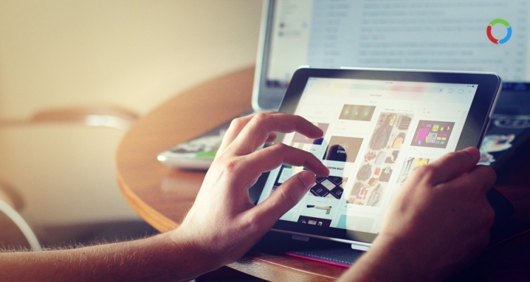 Presença Digital - Logomotiva - Imagem que mostram as mãos de alguém navegando em uma interface digital em um tablet com um laptop ao fundo